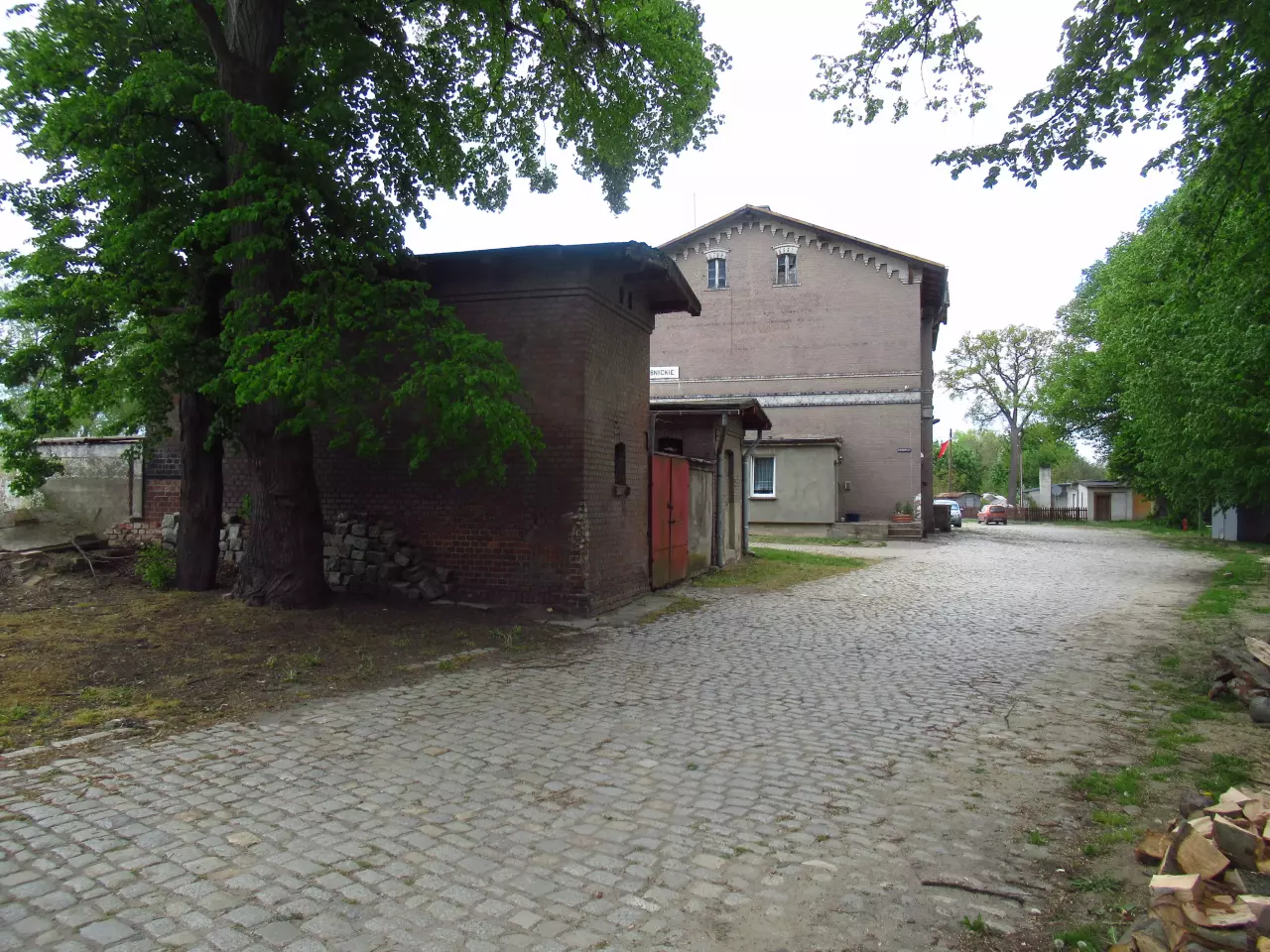 fot. wasiukibic 
Budynek gospodarczy i toalety od strony drogi dojazdowej. W tle budynek dworca. Widok w kierunku północnym. Obraz